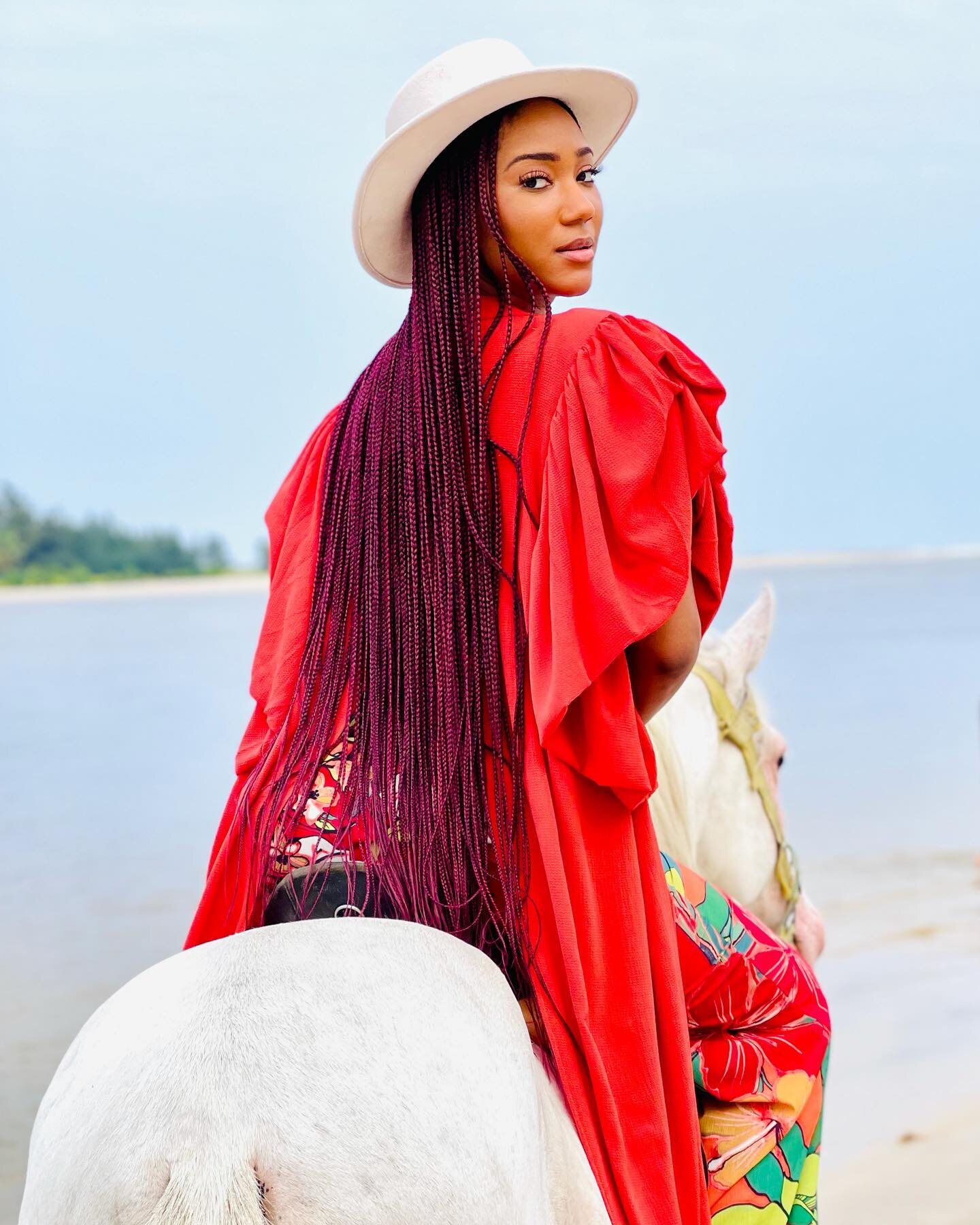Amy Lucia Diop à cheval sur la plage au petit matin, cape rouge et chapeau blanc